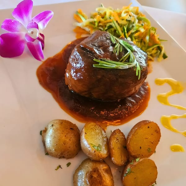 Braised short rib with rosemary, roasted potatoes, and shredded vegetables, garnished with an orchid.