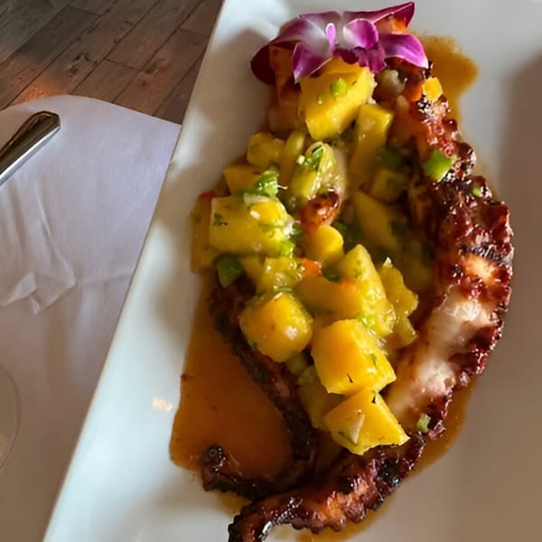Grilled octopus with mango salsa and a purple orchid garnish on a white plate at IXCHEL Mexican Cuisine.