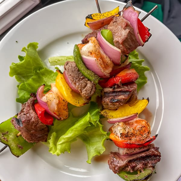 Two skewers of grilled beef, shrimp, and colorful vegetables on a bed of lettuce.