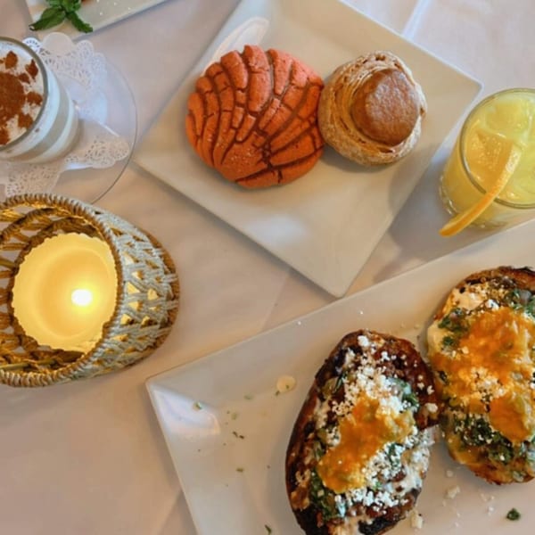 Table with Mexican pastries, orange juice, a dessert, and two loaded baked potatoes with cheese.