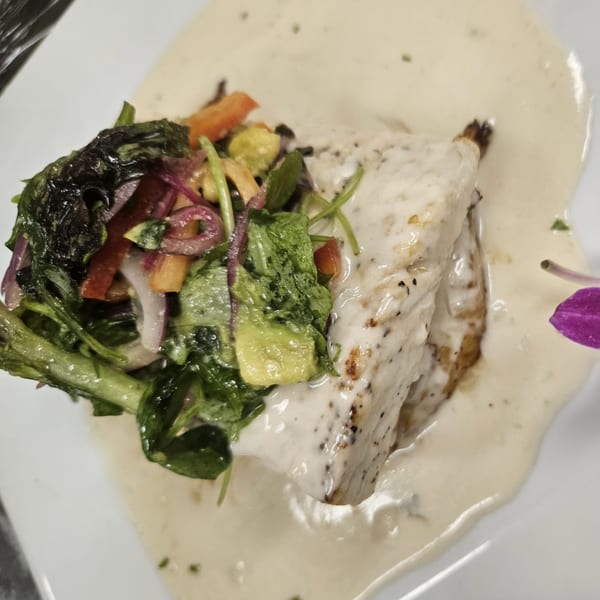 Grilled fish fillet with creamy white sauce, topped with a vibrant salad and a purple orchid.