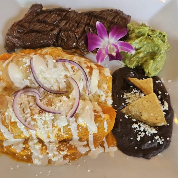 IXCHEL Mexican Cuisine's steak and enchiladas with black beans, guacamole, and a purple orchid.