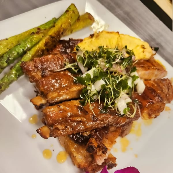 IXCHEL Mexican Cuisine's glazed ribs with grilled asparagus, pineapple, and microgreens on a white plate.