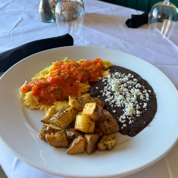 A Mexican breakfast plate with scrambled eggs, salsa, black beans with cheese, and roasted potatoes.