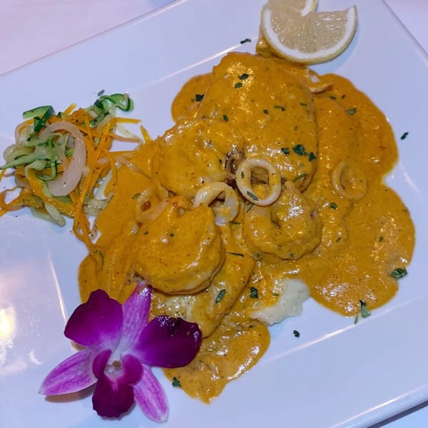 IXCHEL Mexican Cuisine's seafood dish with a rich orange sauce, lemon, and a purple orchid garnish.