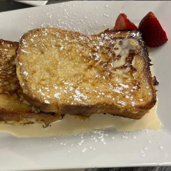 Golden brown French toast slices with powdered sugar, cream, and two strawberry halves on a white plate.