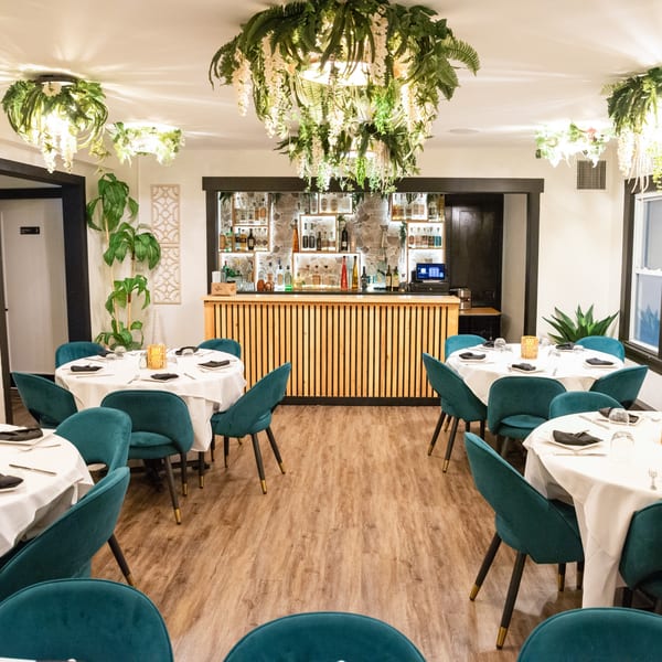 Elegant dining room at IXCHEL Mexican Cuisine with teal chairs, white tablecloths, and a full bar.
