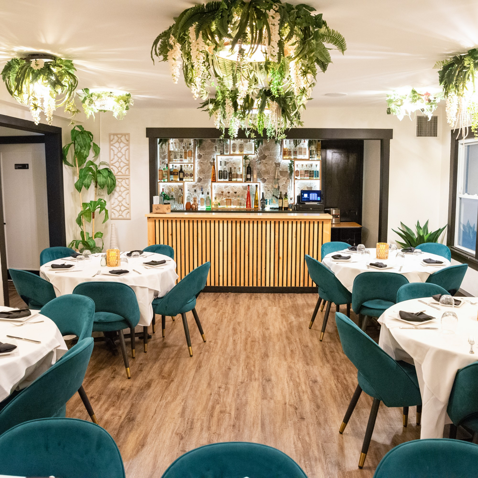 Elegant dining room at IXCHEL Mexican Cuisine with teal chairs, white tablecloths, and a full bar.