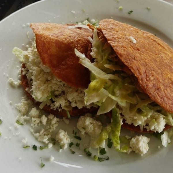 Two Mexican gorditas filled with shredded lettuce and crumbled white cheese on a white plate.