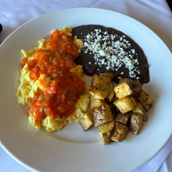 Scrambled eggs with red salsa, black beans with cheese, and roasted potatoes on a white plate.