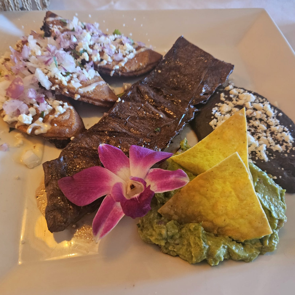 IXCHEL Mexican Cuisine's carne asada with guacamole, chips, black beans, and sopes, garnished with an orchid.