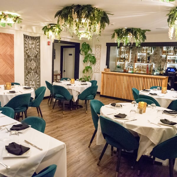 Elegant dining room at IXCHEL Mexican Cuisine with teal chairs, white tablecloths, and a full bar.