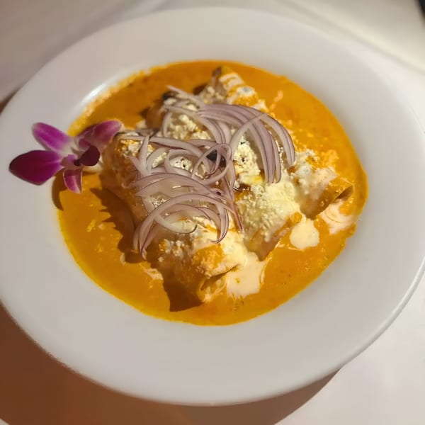 IXCHEL Mexican Cuisine's enchiladas in orange sauce, topped with cheese, red onions, and a purple orchid.